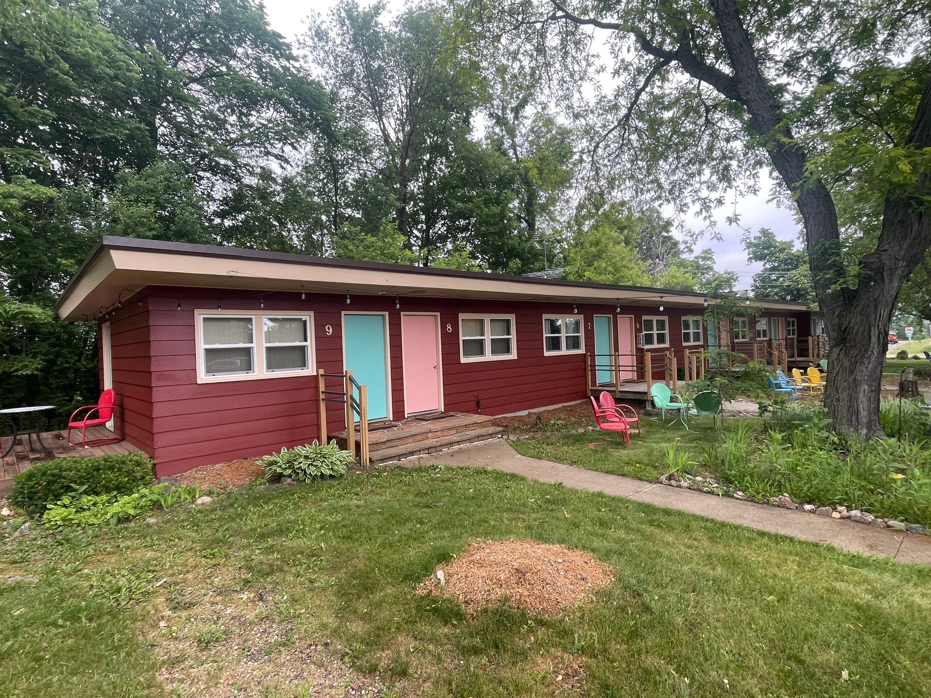A row of small, red motel rooms with colorful doors, set in a grassy area with trees.