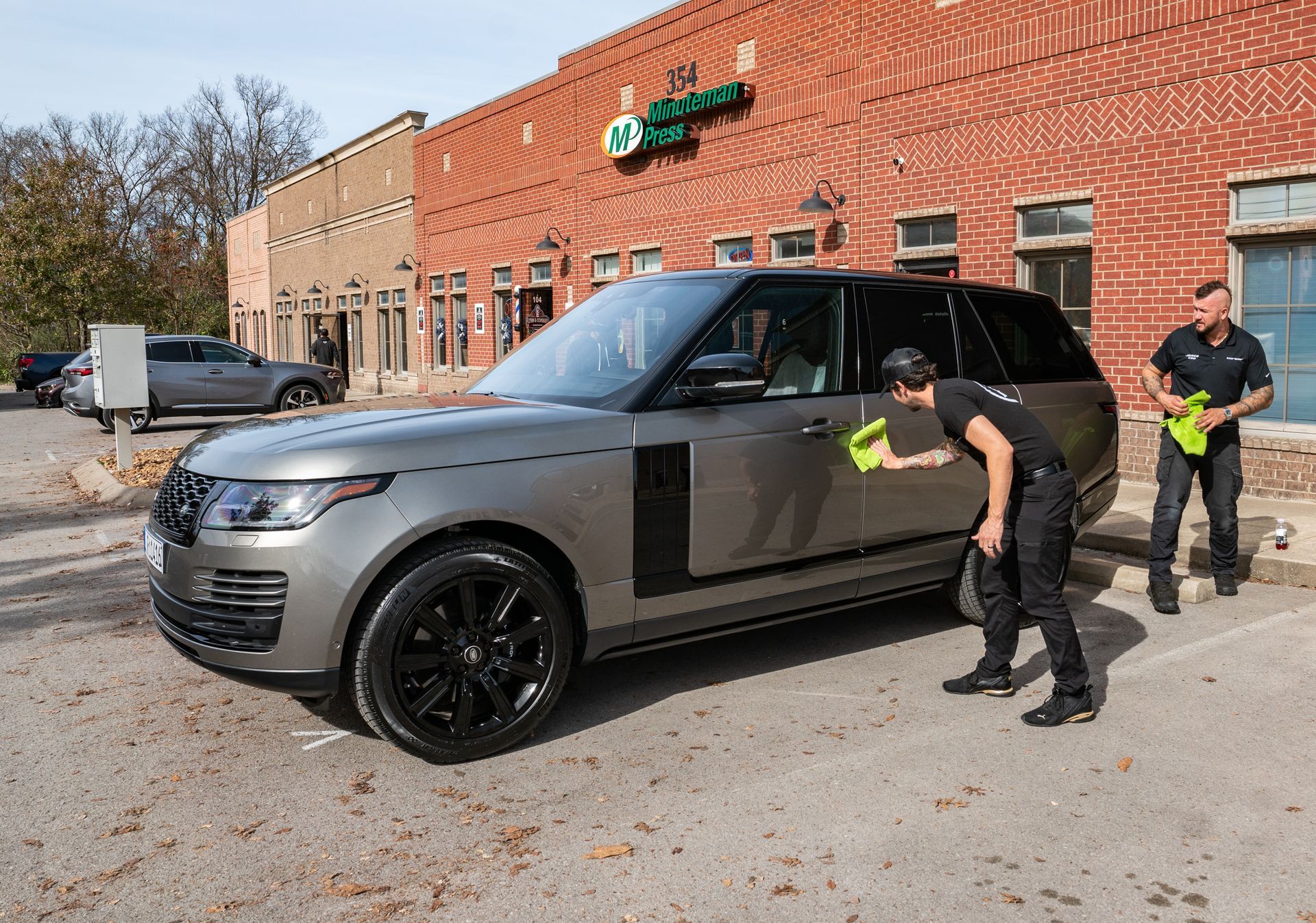 Two men are cleaning a range rover parked in front of a brick building.
