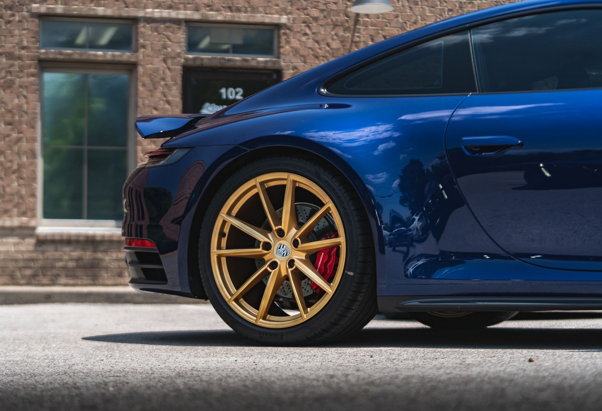 A blue sports car with gold wheels is parked in front of a brick building.