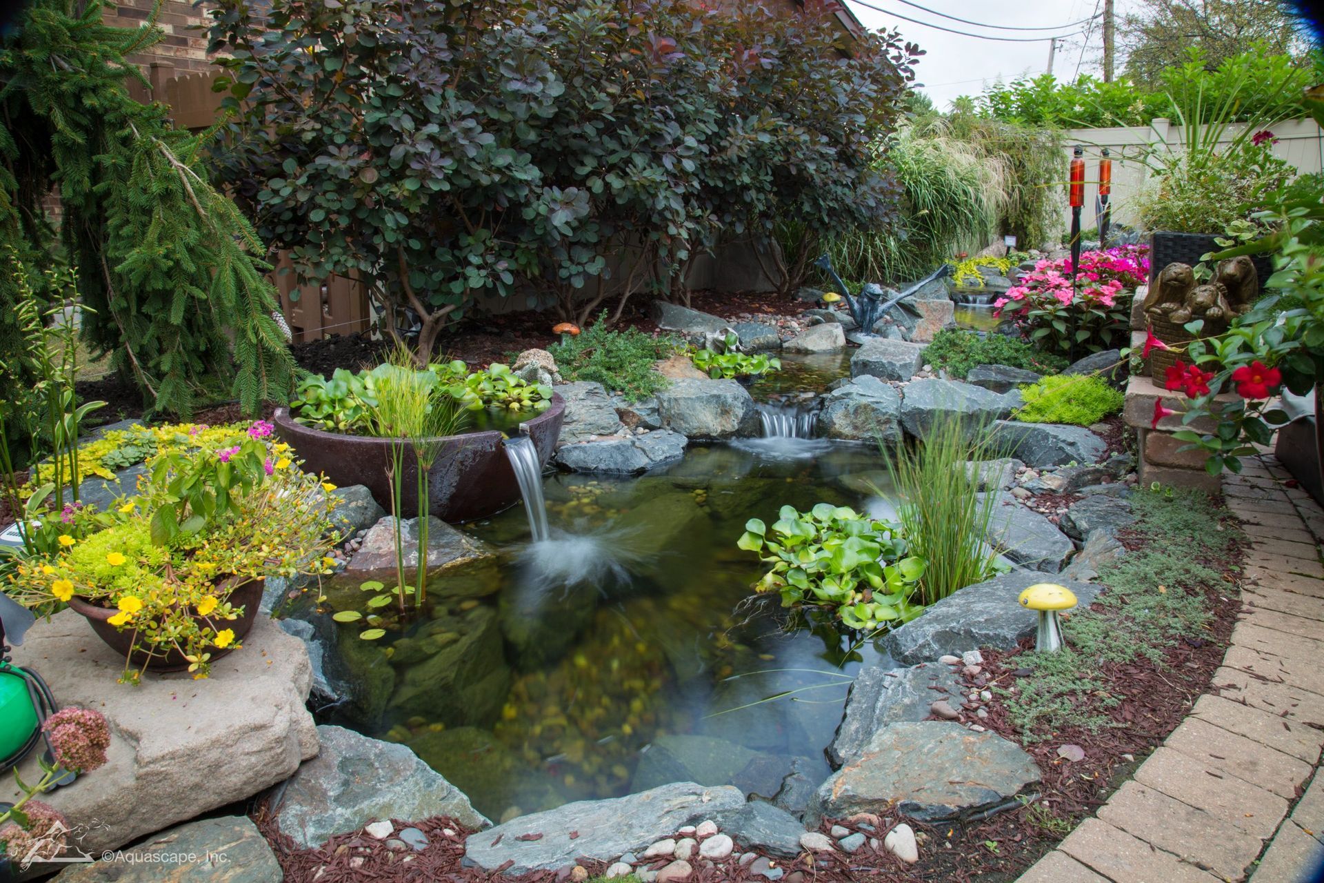 A lush garden pond with waterfall, surrounded by rocks and colorful flowers.