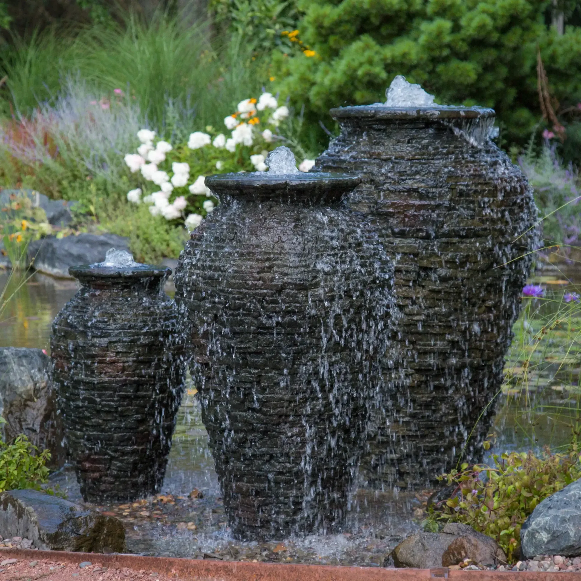 Three tiered waterfall fountains in a garden pond. Dark stone texture, water cascading down.