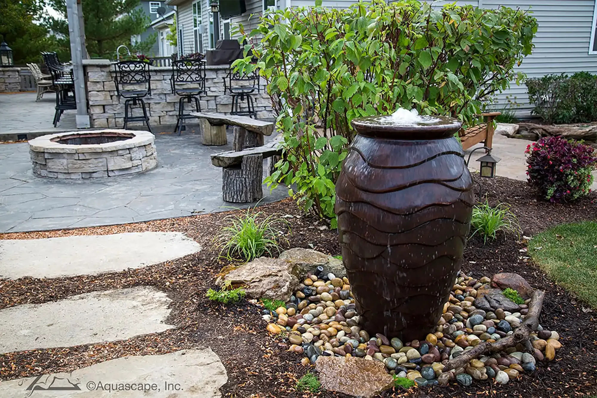 Backyard patio with fire pit, water fountain, and seating area.