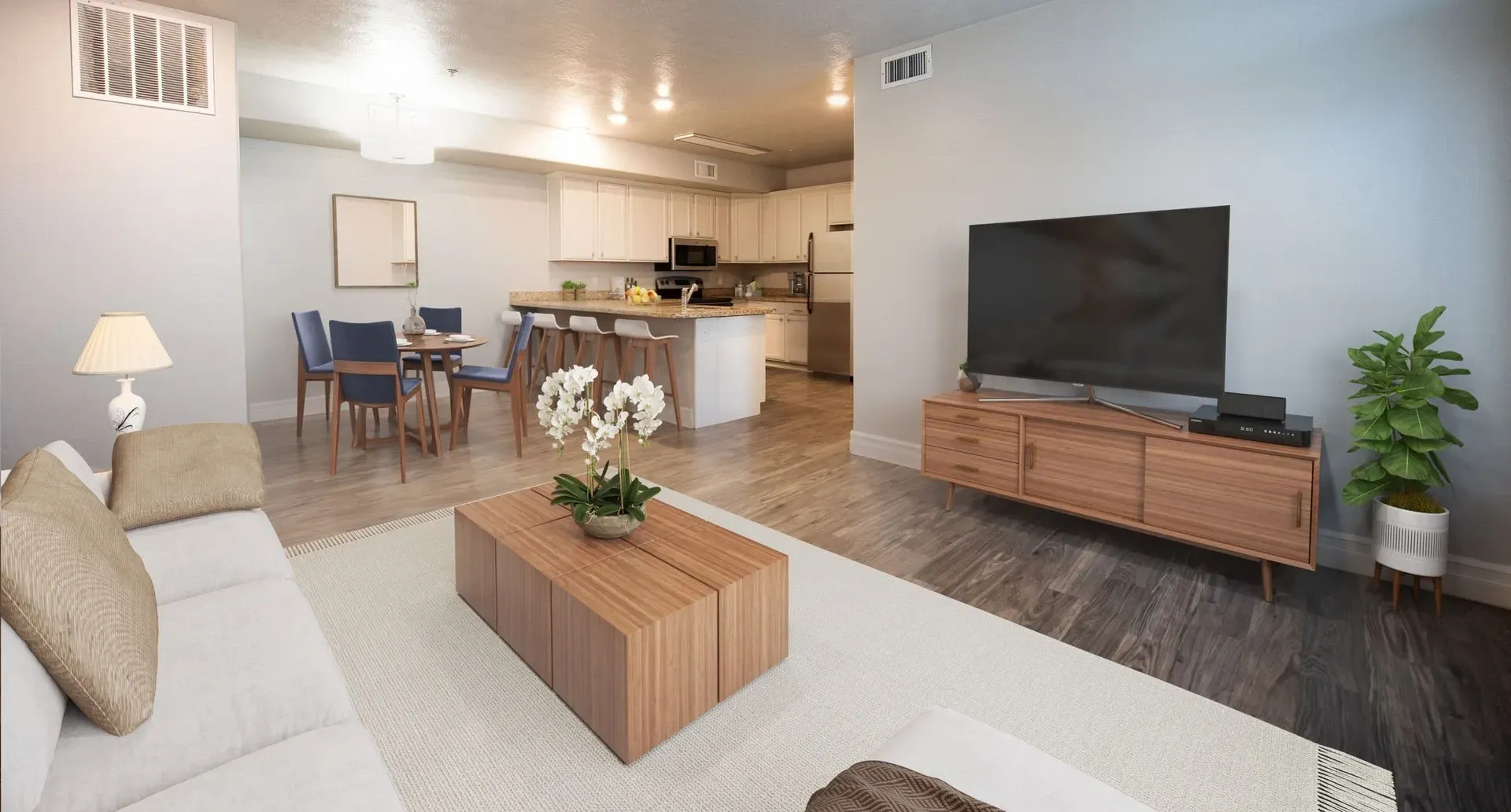 Living room with a couch, coffee table, TV, and dining area adjacent to the kitchen at Hills at Renaissance, offering apartments for rent in Bountiful, UT.