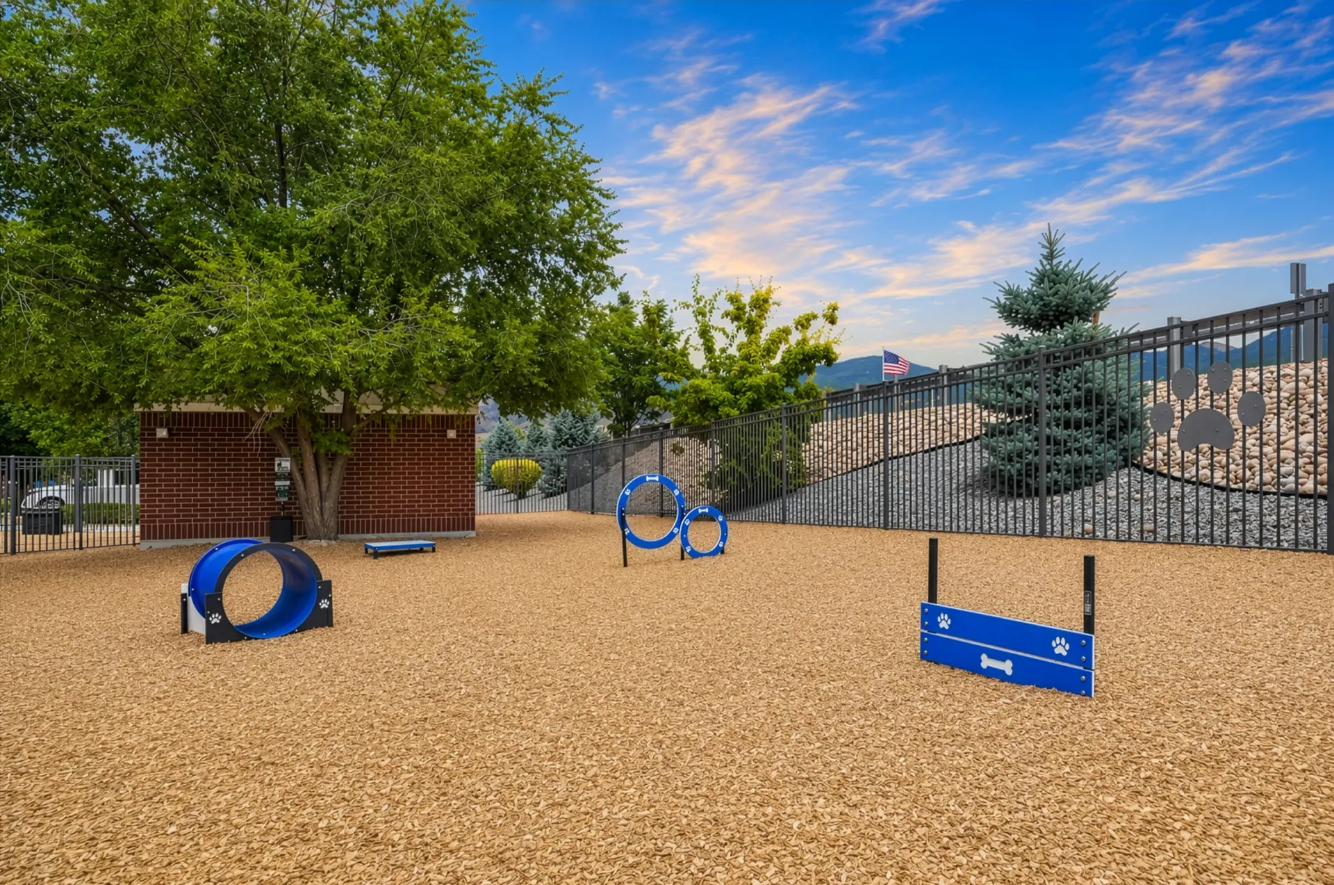 Dog park with agility equipment and a brick building at Hills at Renaissance, offering pet-friendly apartments in Bountiful, UT.