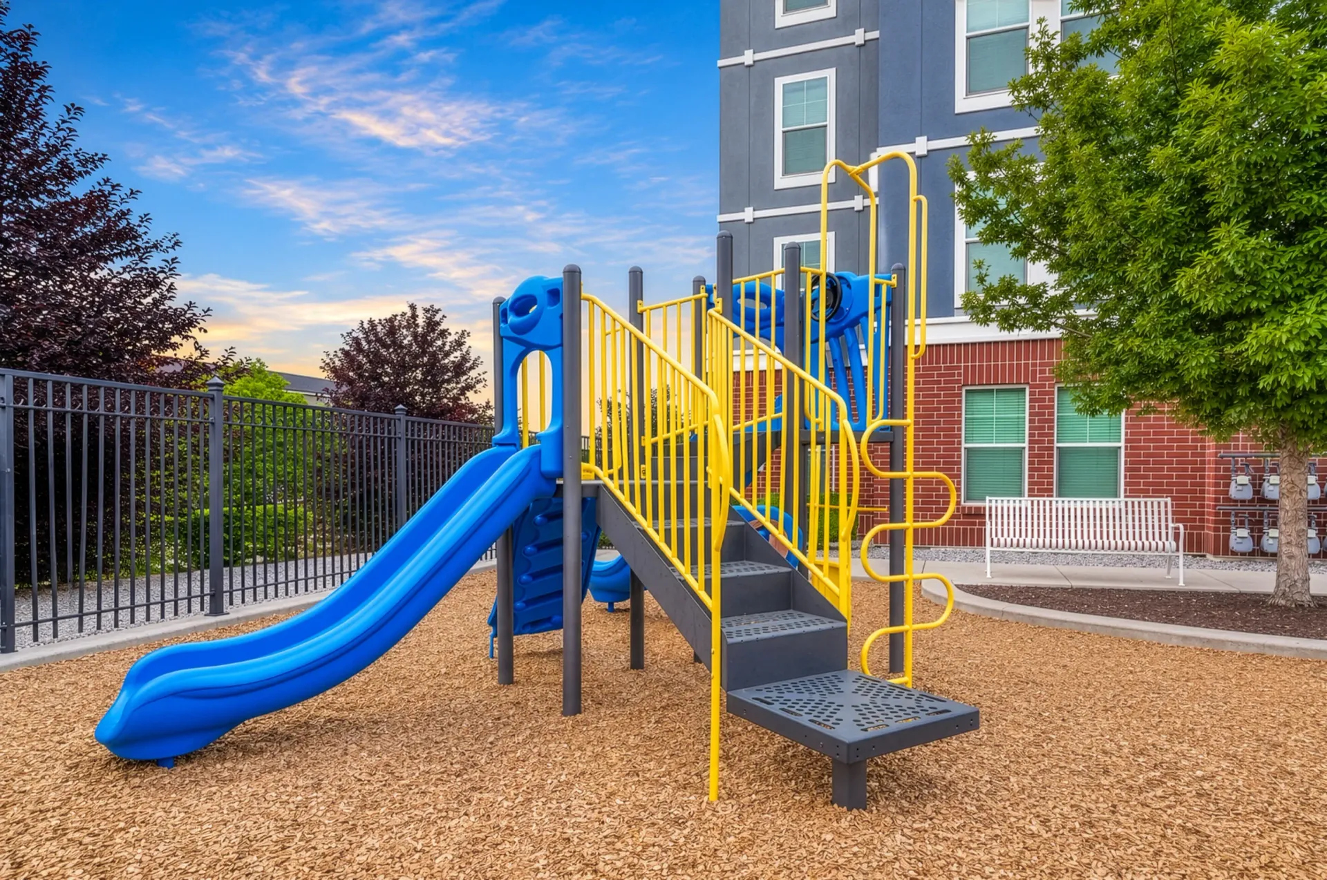 Playground with blue and yellow slide and stairs, adjacent to apartment buildings at Hills at Renaissance, offering apartments in Bountiful, UT.