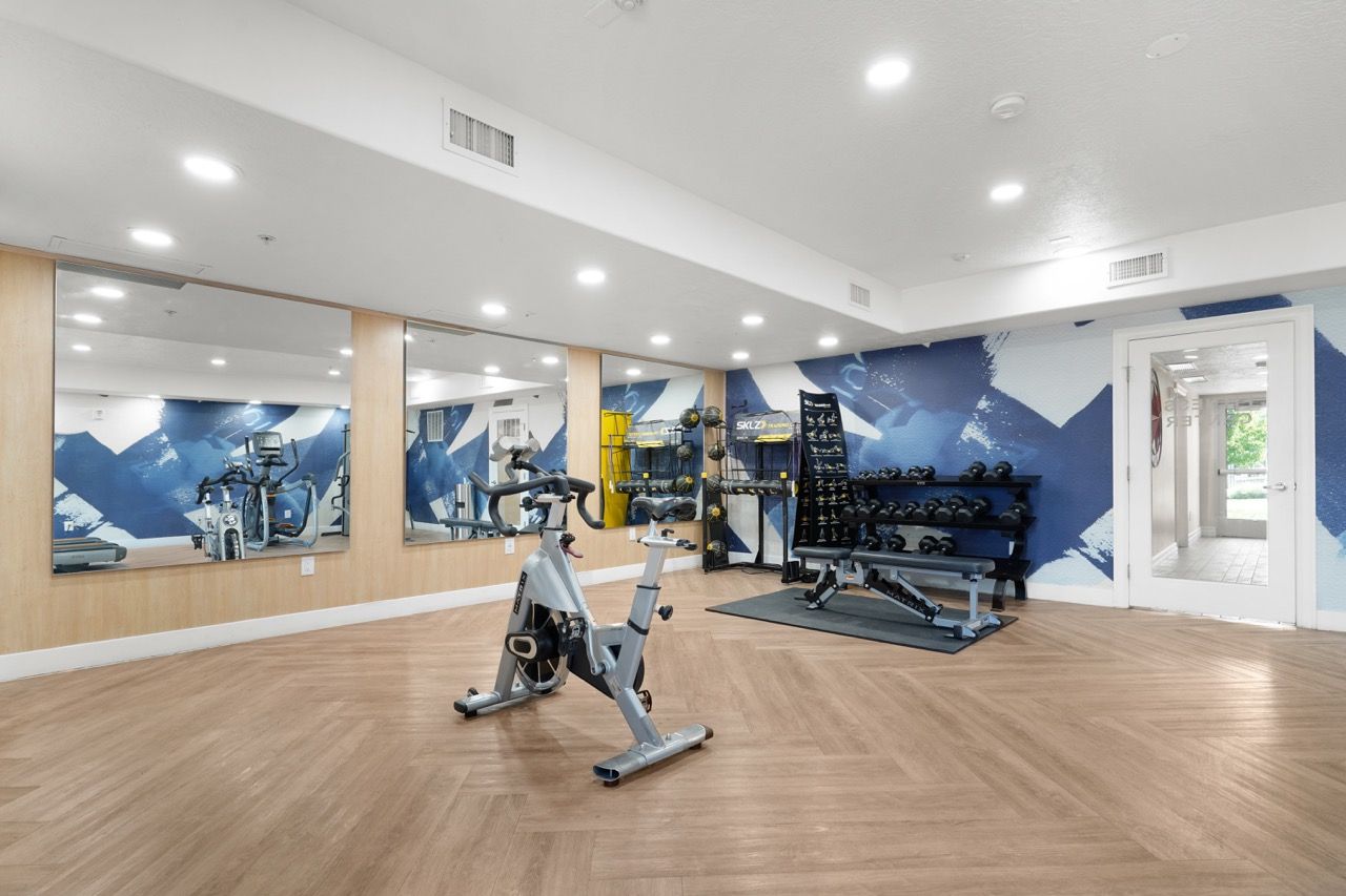 Hills at Renaissance apartment gym with cardio bike, free weights, and mirrored wall.