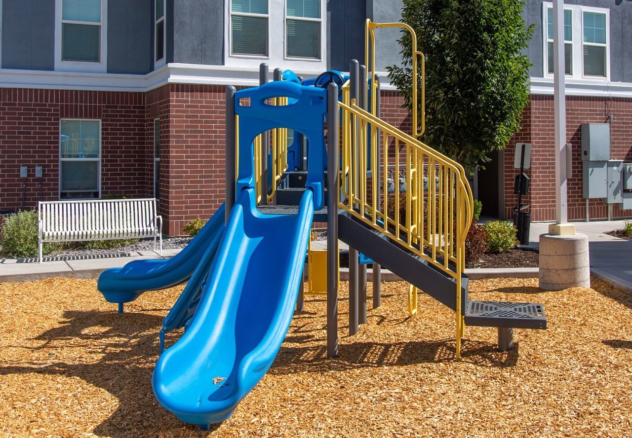Hills at Renaissance playground with slides and yellow railings in a courtyard beside an apartment building.