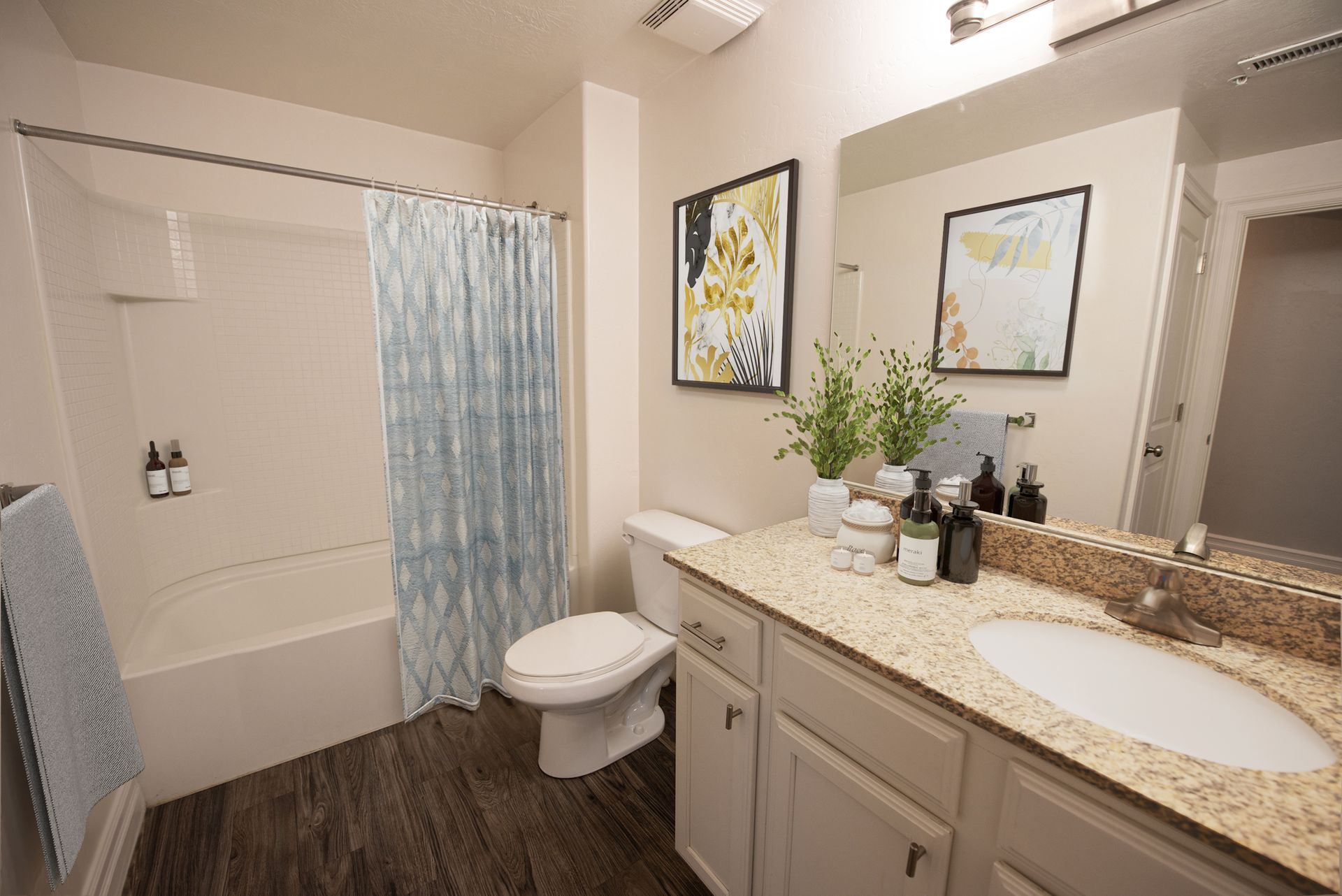 Hills at Renaissance Bathroom with light wood cabinets, granite countertop, white sink, and shower/tub with blue curtain.
