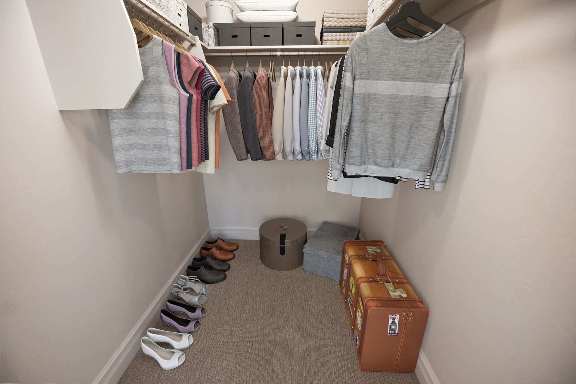 Hills at Renaissance walk-in closet with clothes hanging. Shoes and a trunk are on the floor. Beige walls and carpet.