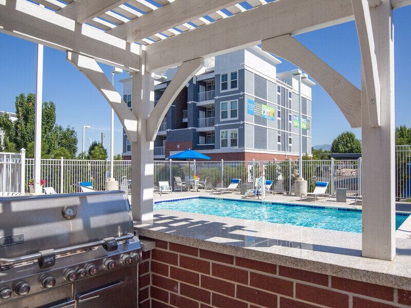 Hills at Renaissance pool area with a grill under a pergola and lounge chairs, with an apartment building in the background.