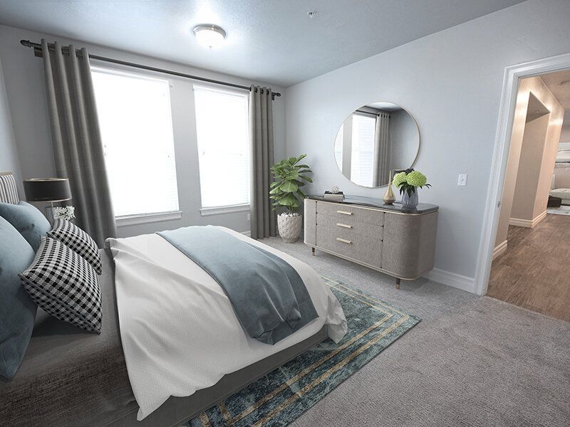 Hills at Renaissance Bedroom in a modern apartment with a king bed, grey dresser, round mirror, potted plant, and two light-filled windows.