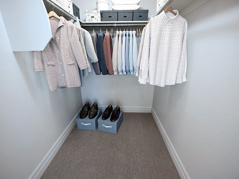 Hills at Renaissance walk-in closet with clothes on hangers, shoe boxes on floor, and storage bins on top shelf.
