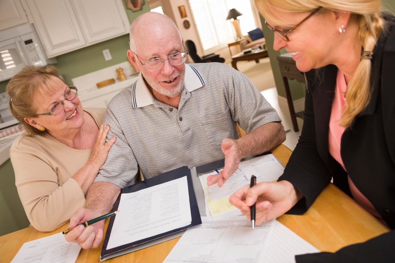 Three people reviewing paperwork at a kitchen table, talking and writing together