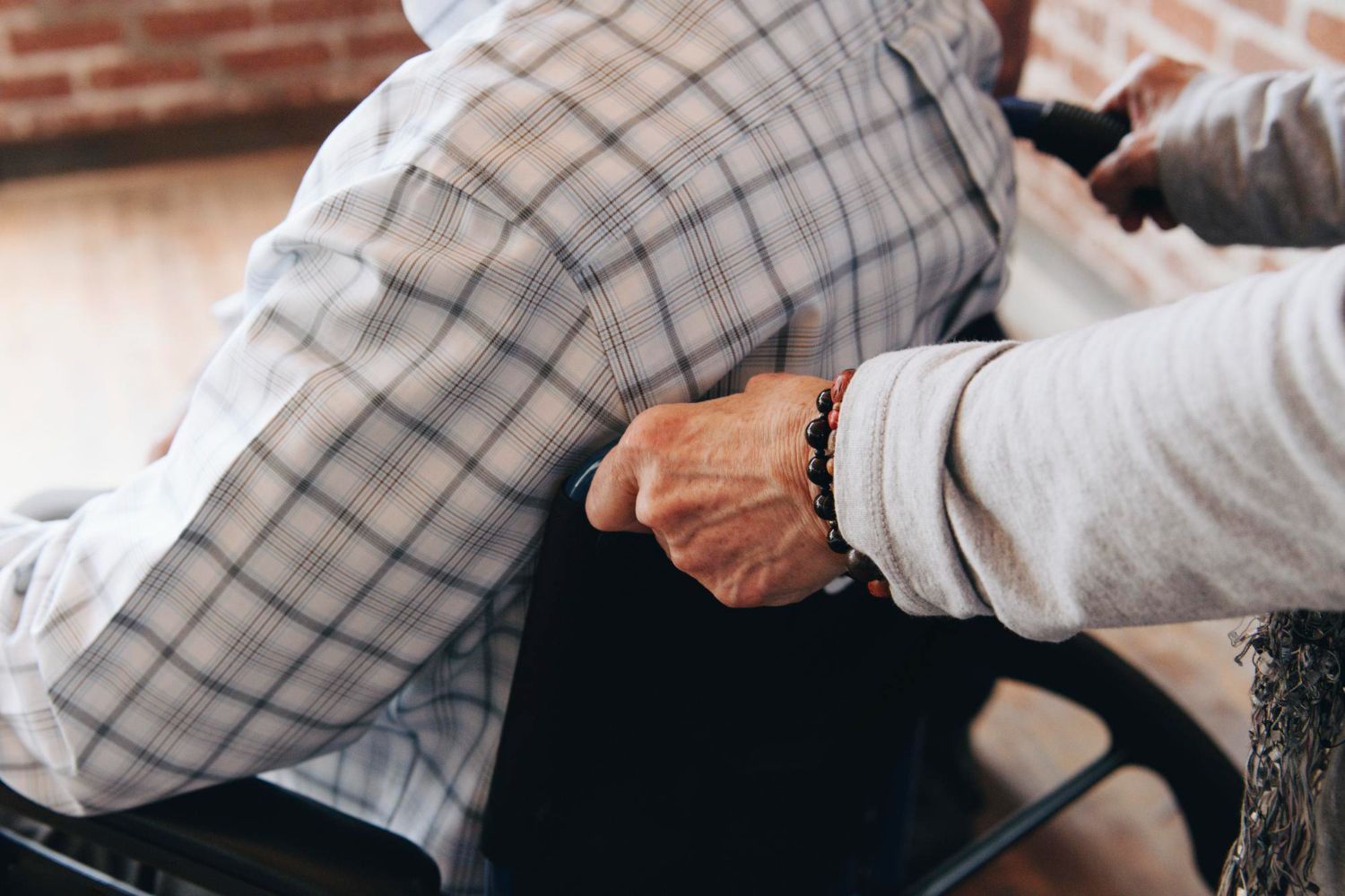 Close-up of hands adjusting a seated person’s plaid jacket in a workshop-like setting