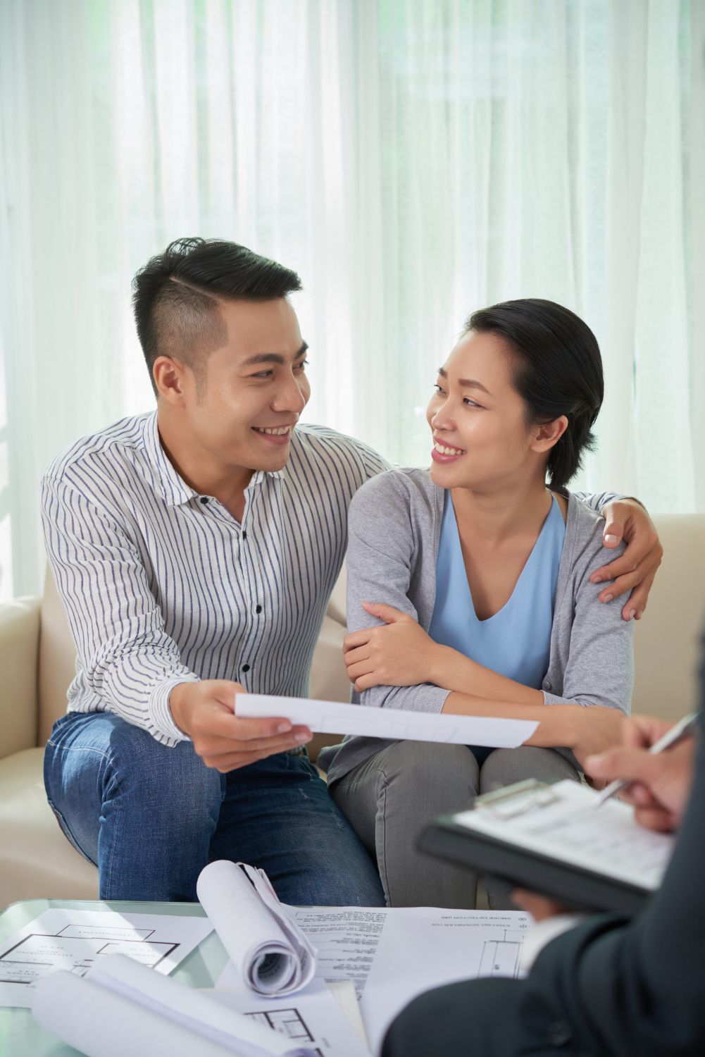 Couple smiling and reviewing documents with a realtor at a table in a bright office