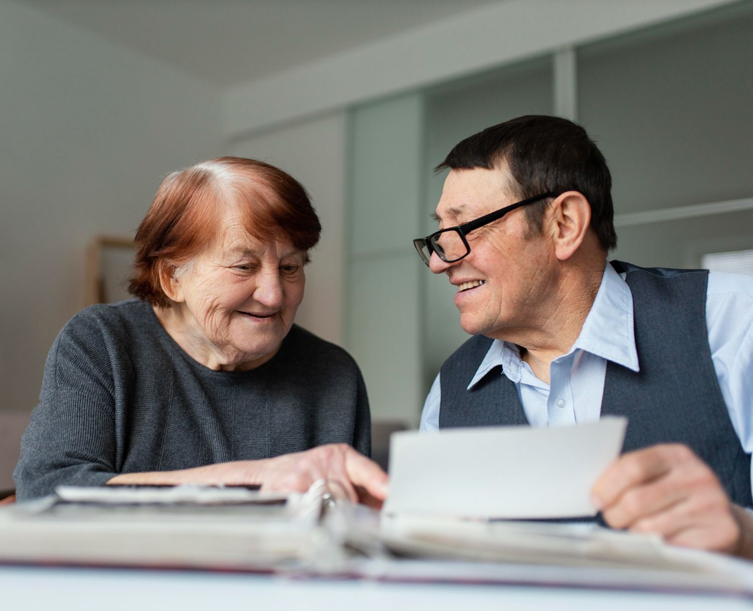 Two people smiling and talking over papers at a table in a bright room