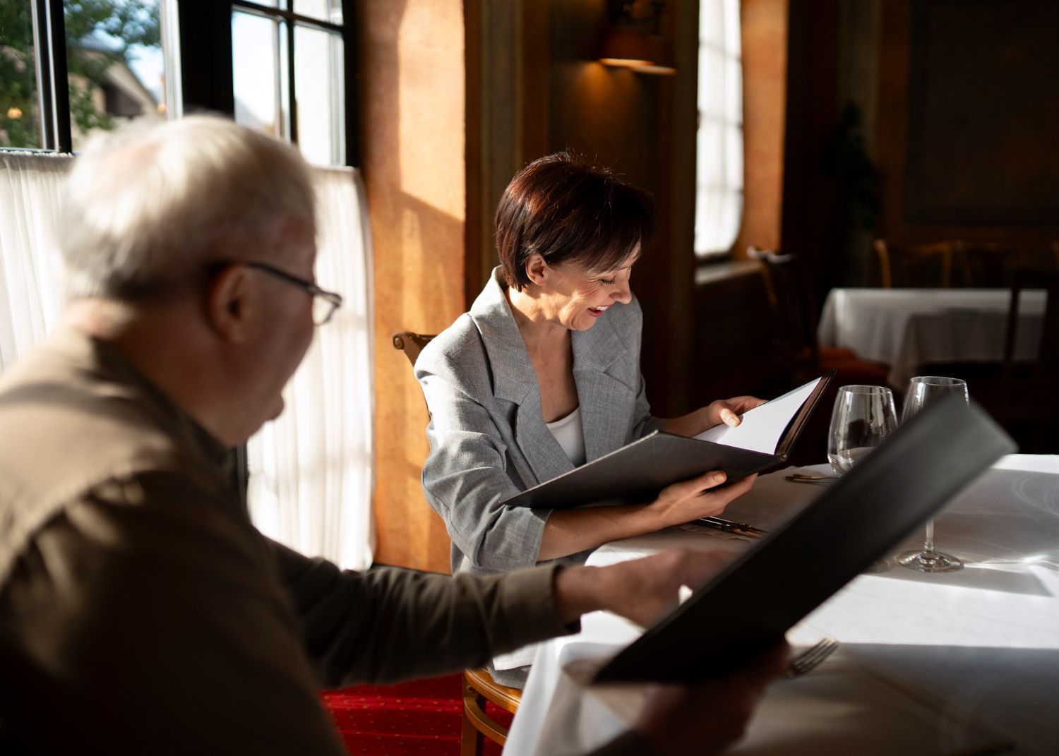 Two people seated at a sunlit table, reading music folders by a window.