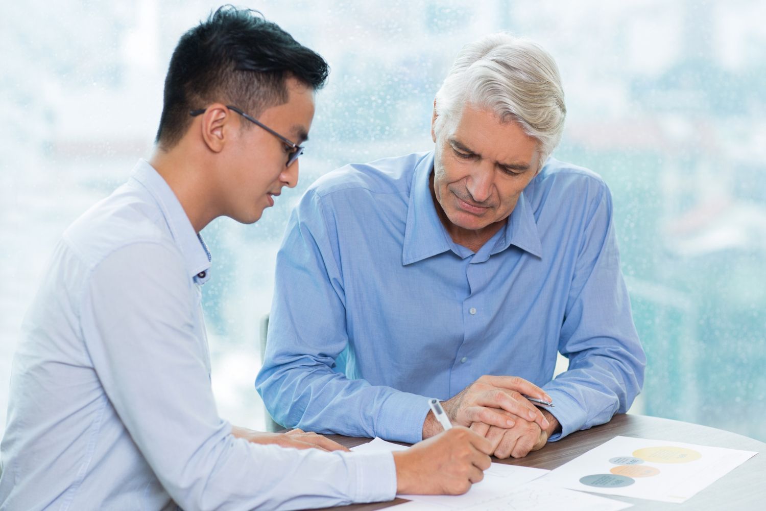Two people in blue shirts reviewing charts together at a desk in a bright office.