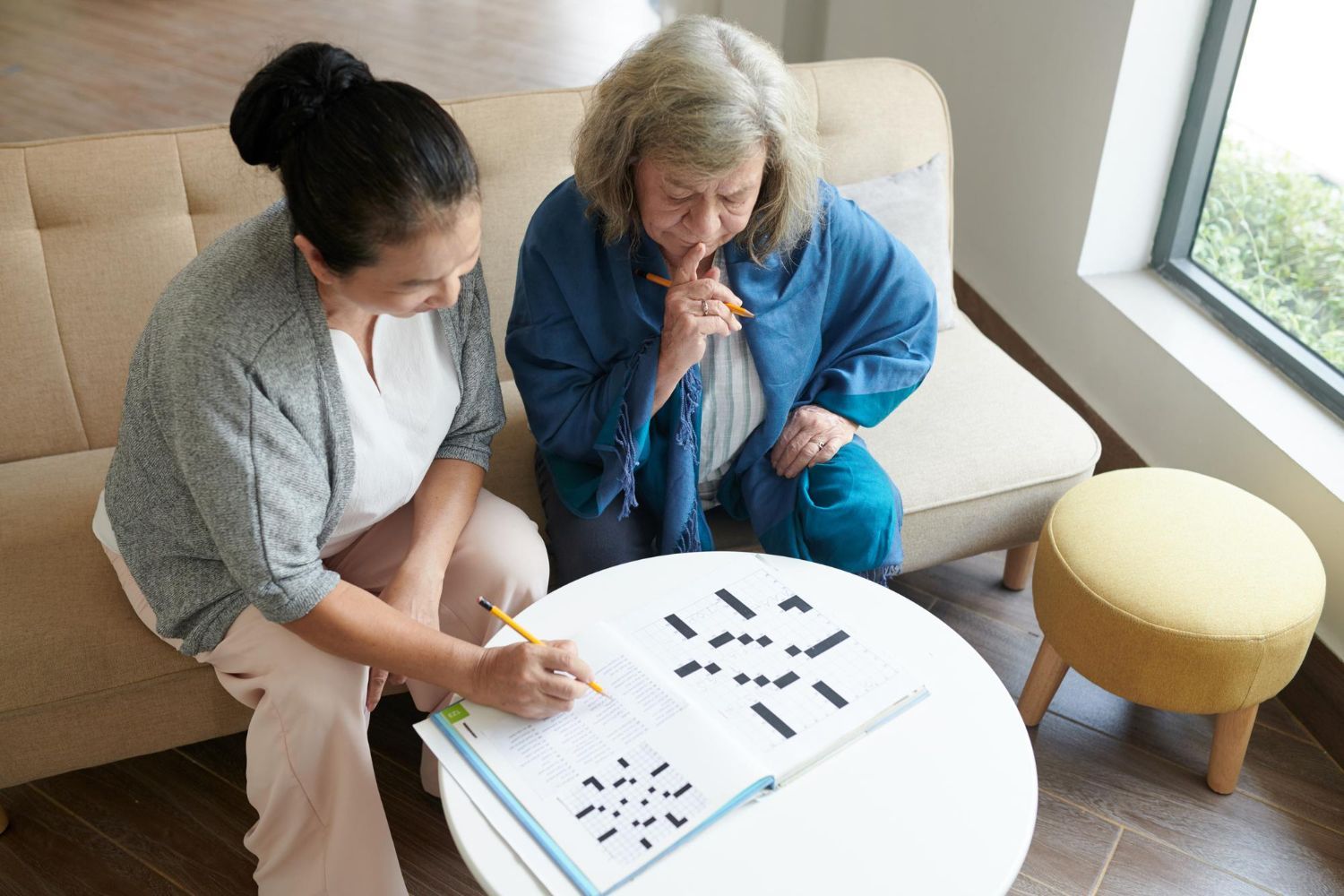 Two women playing a tile game at a small table in a bright living room