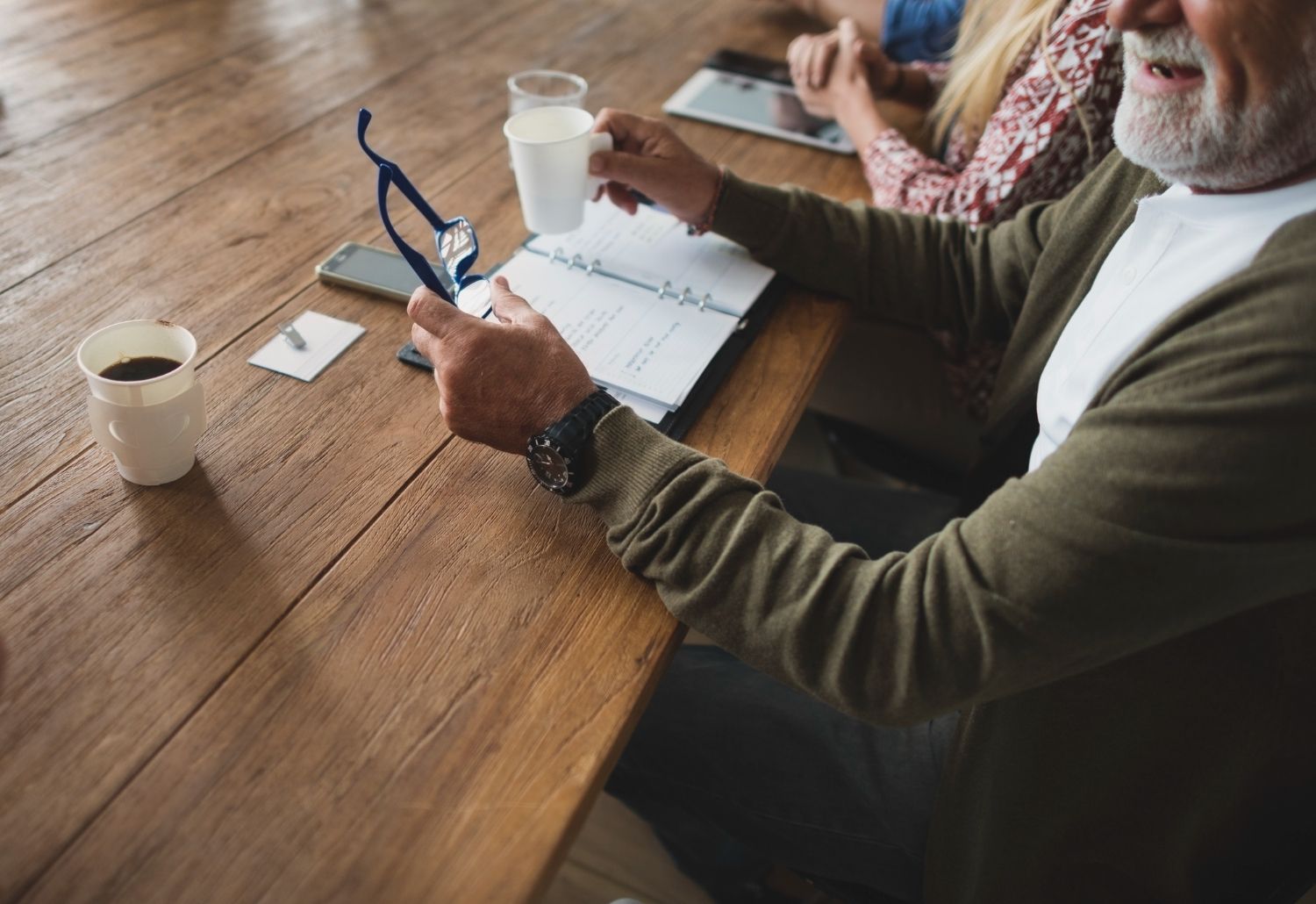 People at a wooden table holding glasses and talking over an open notebook