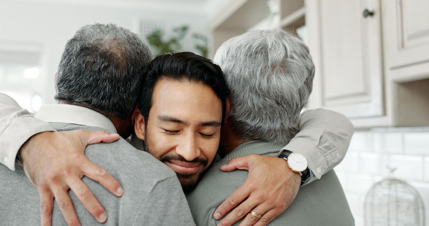 Three people embracing in a warm hug in a bright kitchen