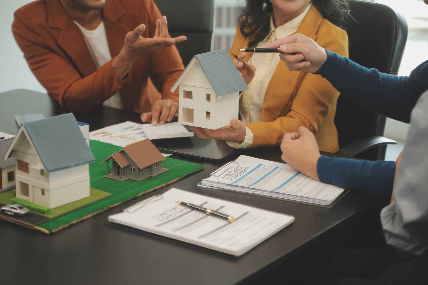 People reviewing small house models and floor plans on a table in a real estate meeting