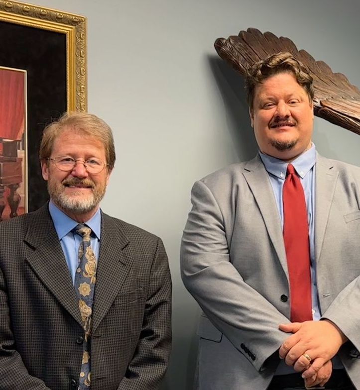 Two men in suits standing indoors, one wearing a blue tie and the other a red tie.
