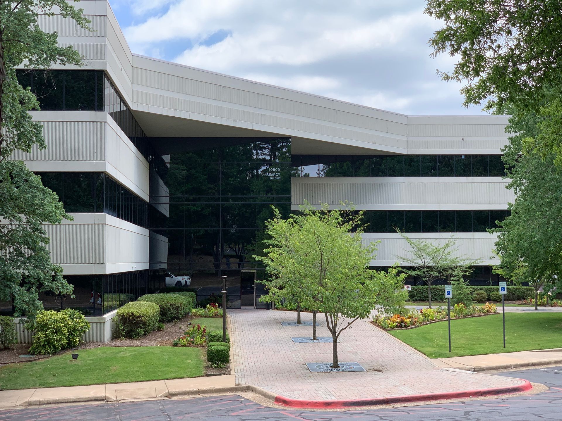 Modern office building with curved facade, glass entrance, and landscaped courtyard with a young tree.
