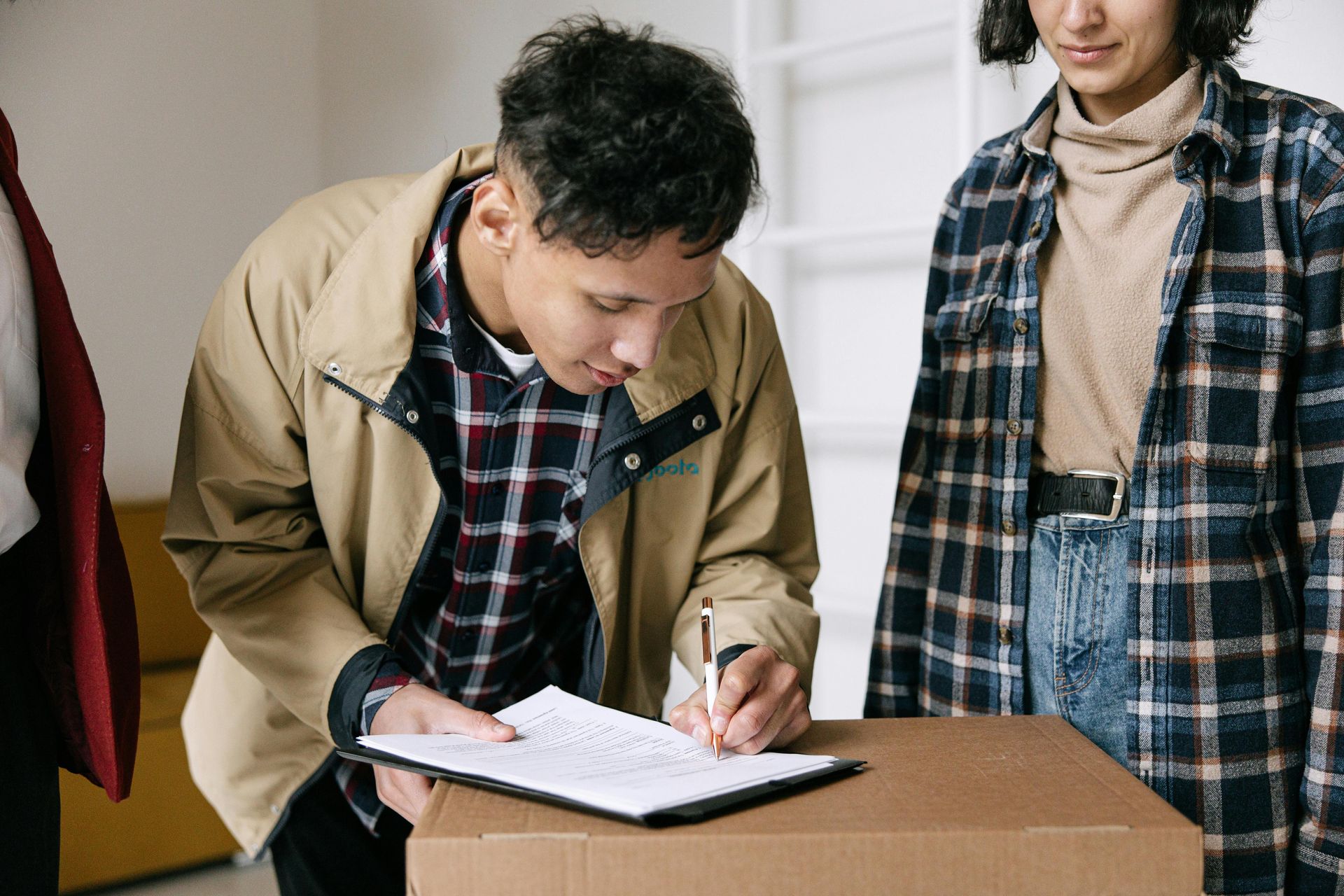 Man signing a clipboard at a table while another person stands nearby indoors