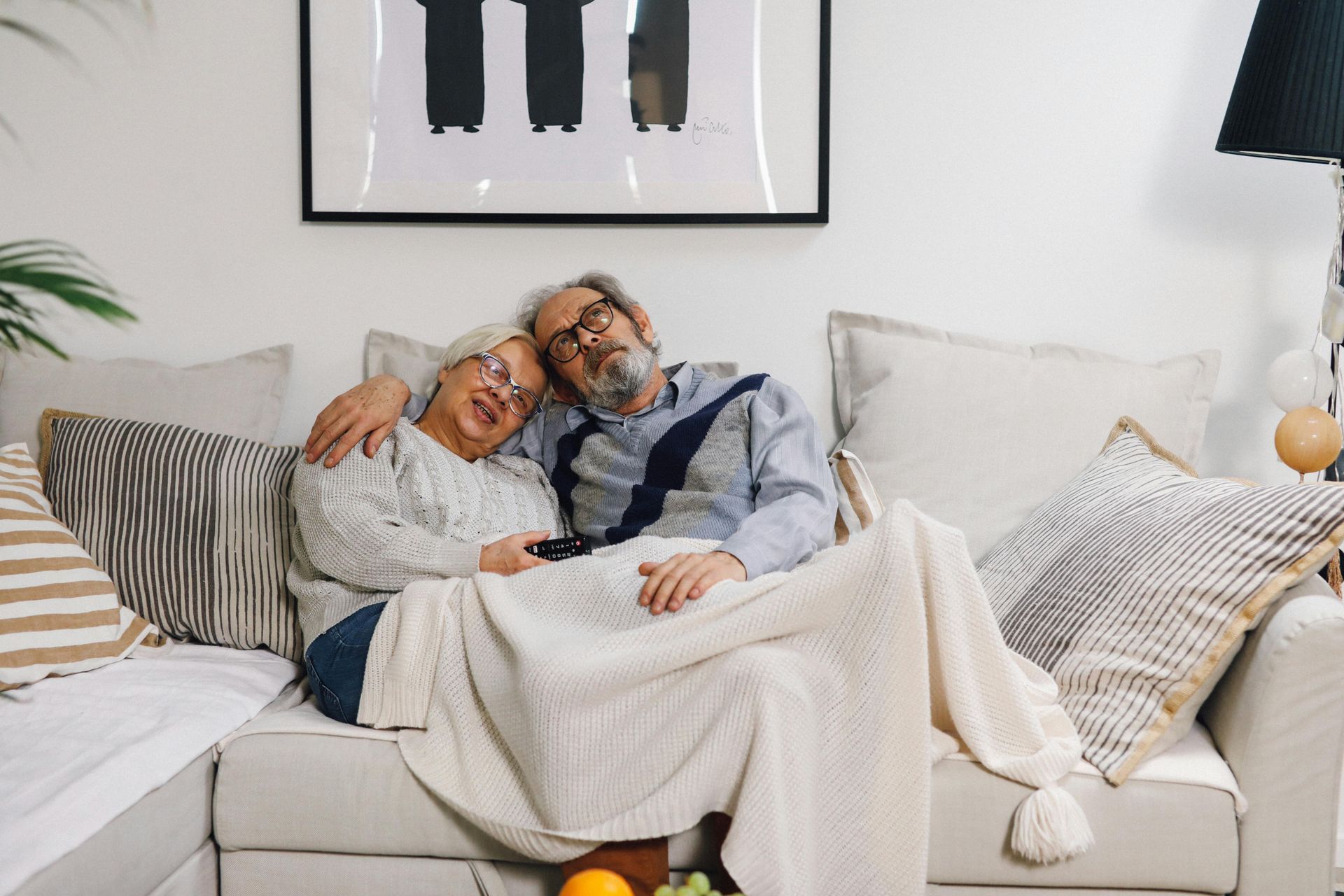 Two people relaxing together on a white couch with pillows in a bright living room