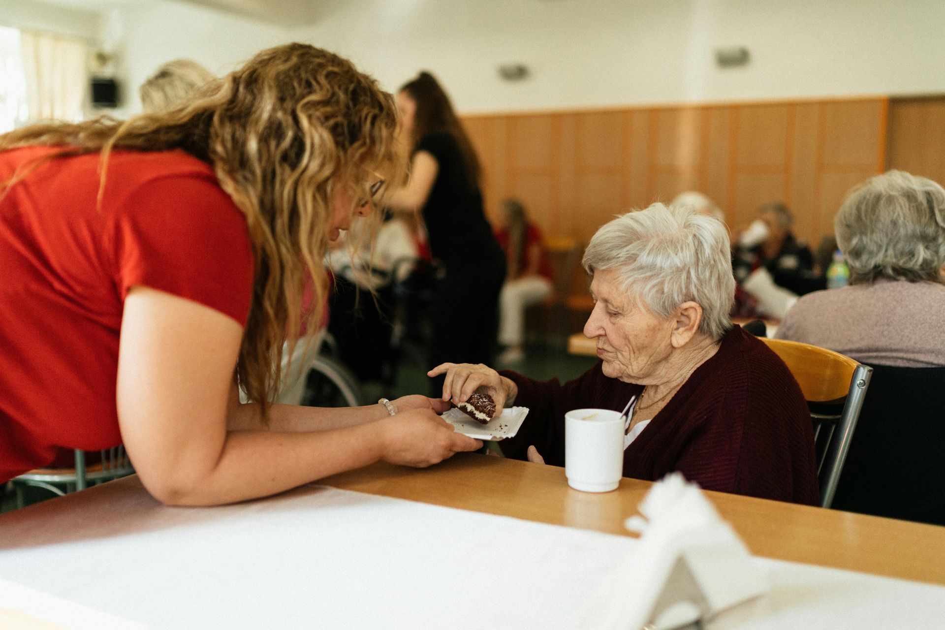 Volunteer assisting an elderly person at a table in a community room