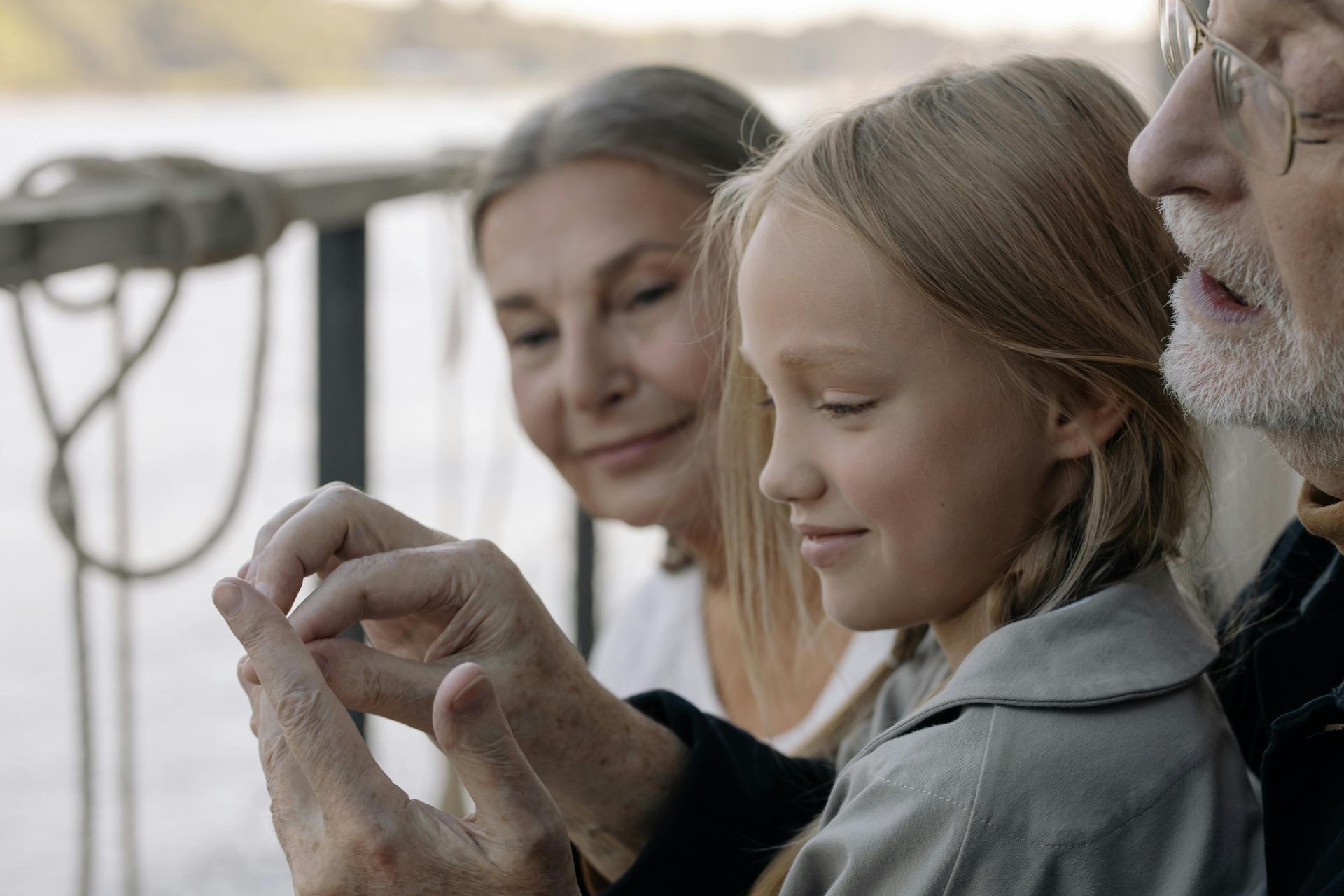 Three people sit outdoors, smiling as they look at a small object held in hand.