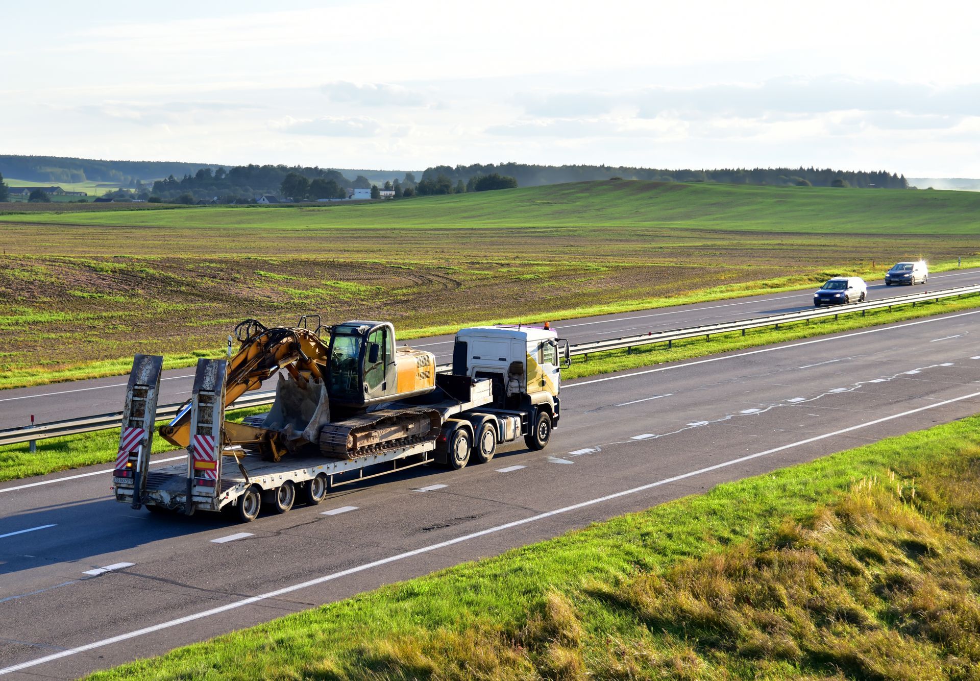 Flatbed tow truck hauling an excavator down a two-lane highway.