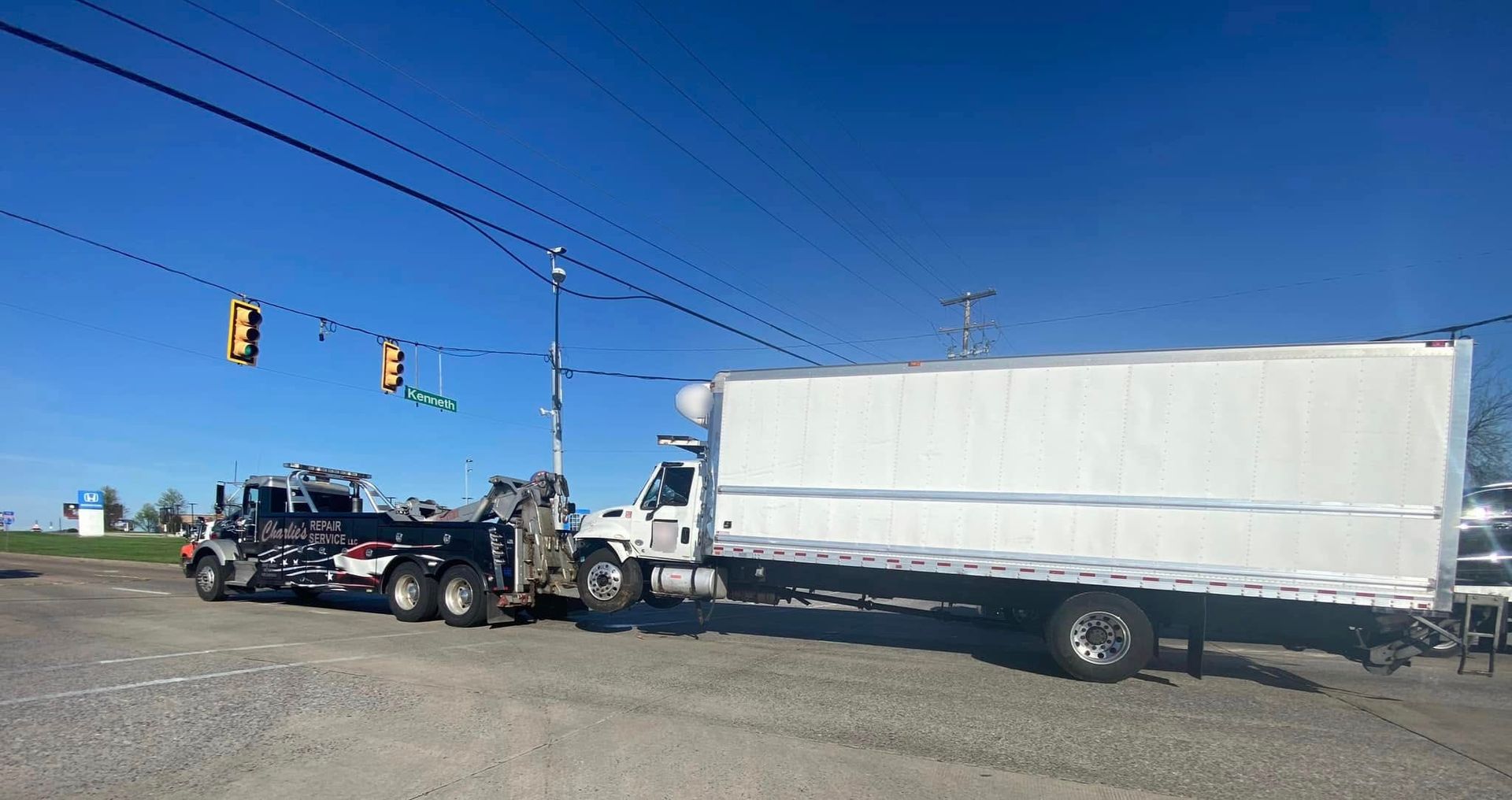 A tow truck towing a large white box truck on a clear, sunny day. A tow truck towing a large white box truck on a clear, sunny day.