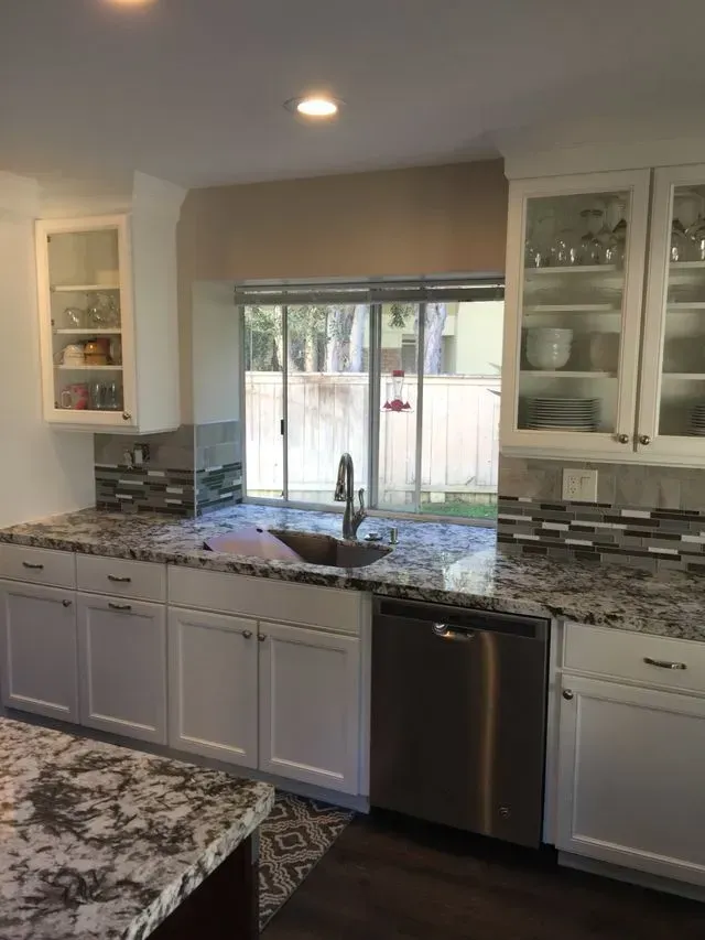 White kitchen with granite countertops, stainless steel appliances, and a window overlooking a yard.