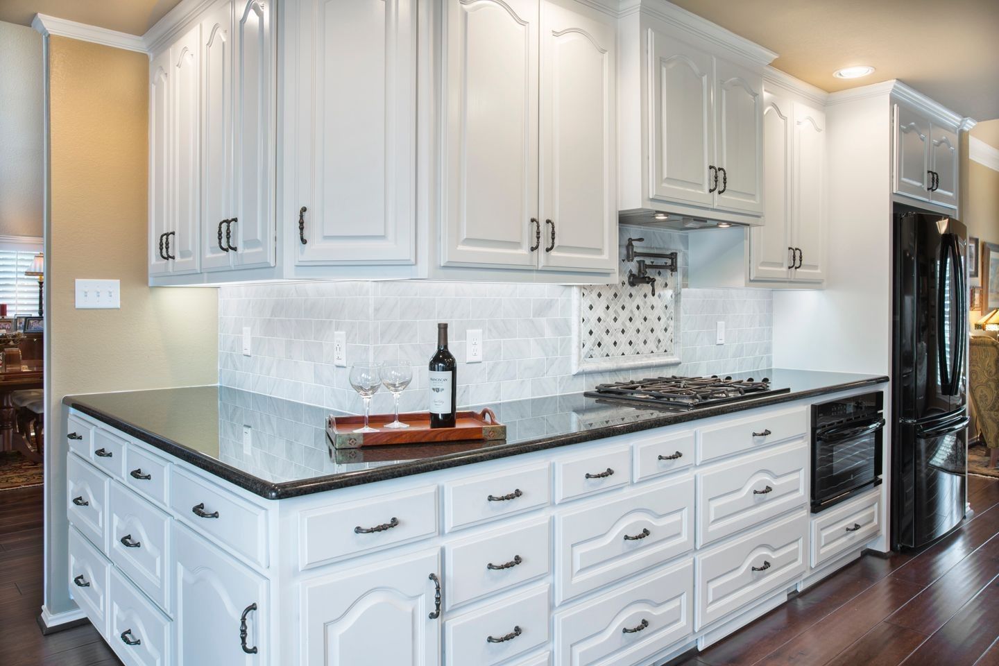 White kitchen cabinets with black countertops and appliances, wooden floor.