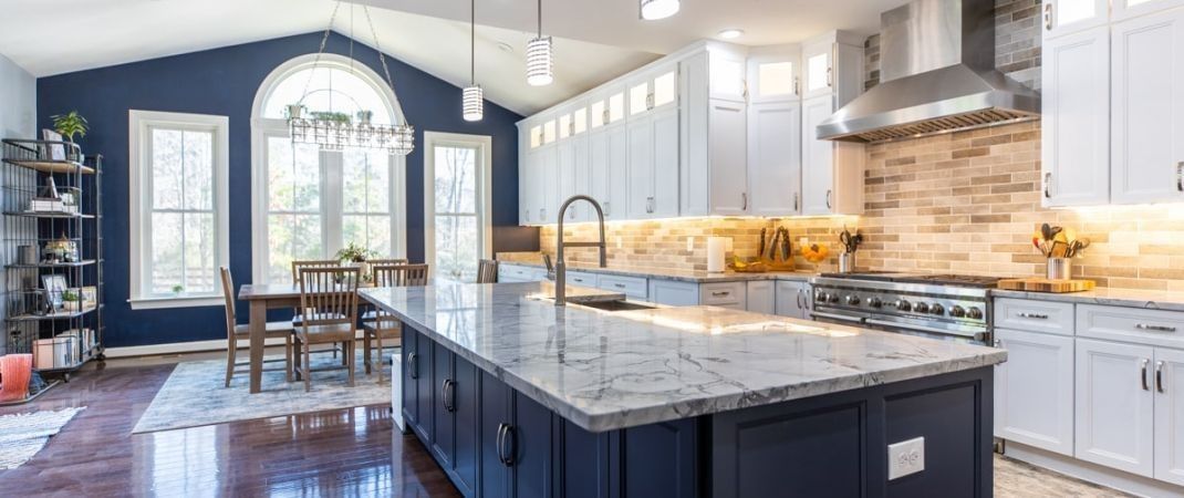 Kitchen with navy blue island and accent wall, white cabinets, and large windows.