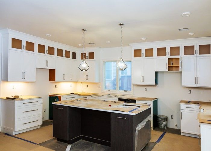 Kitchen under construction with white cabinets, dark island, and unfinished details.