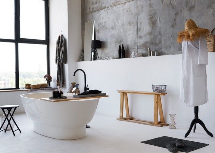 Modern bathroom with a white bathtub, black faucet, and concrete wall. A coat rack and wooden bench are present.