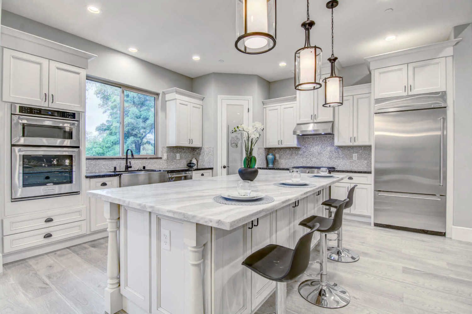 White kitchen with a marble-topped island, stainless steel appliances, and pendant lights.