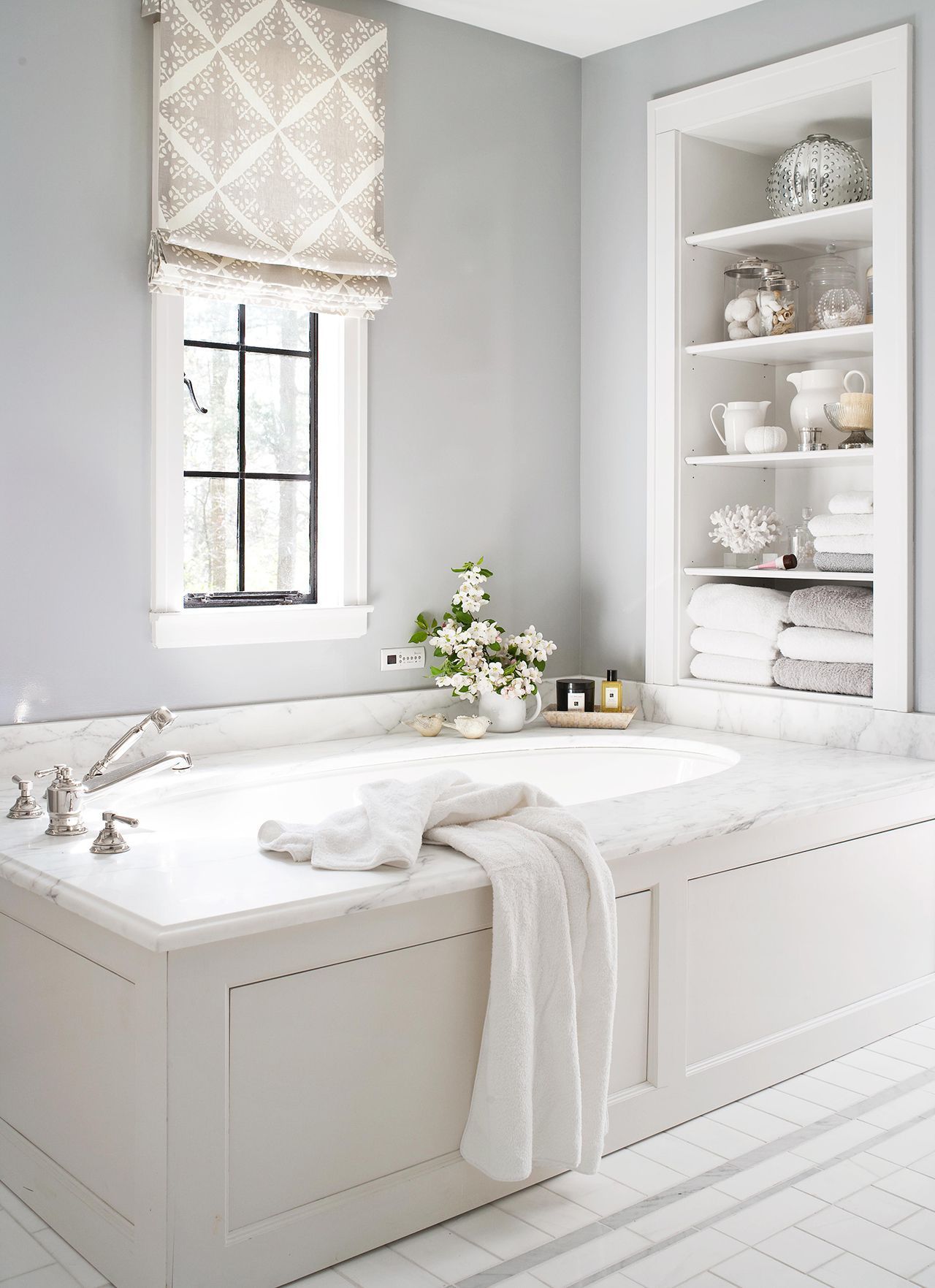 Bathroom with built-in tub, storage niche, window with patterned shade, and white accents, in a light-blue room.