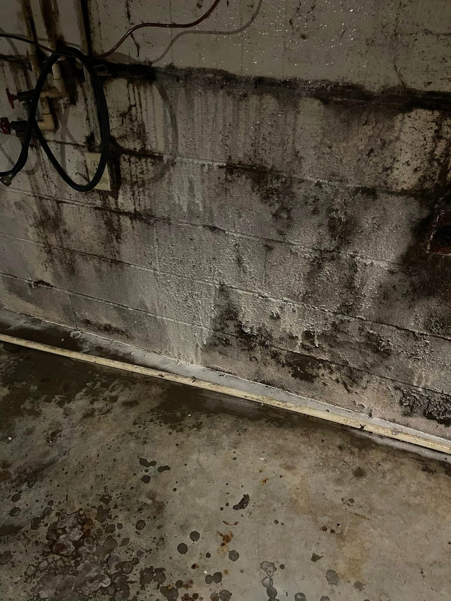 A dirty wall in a basement with a concrete floor.