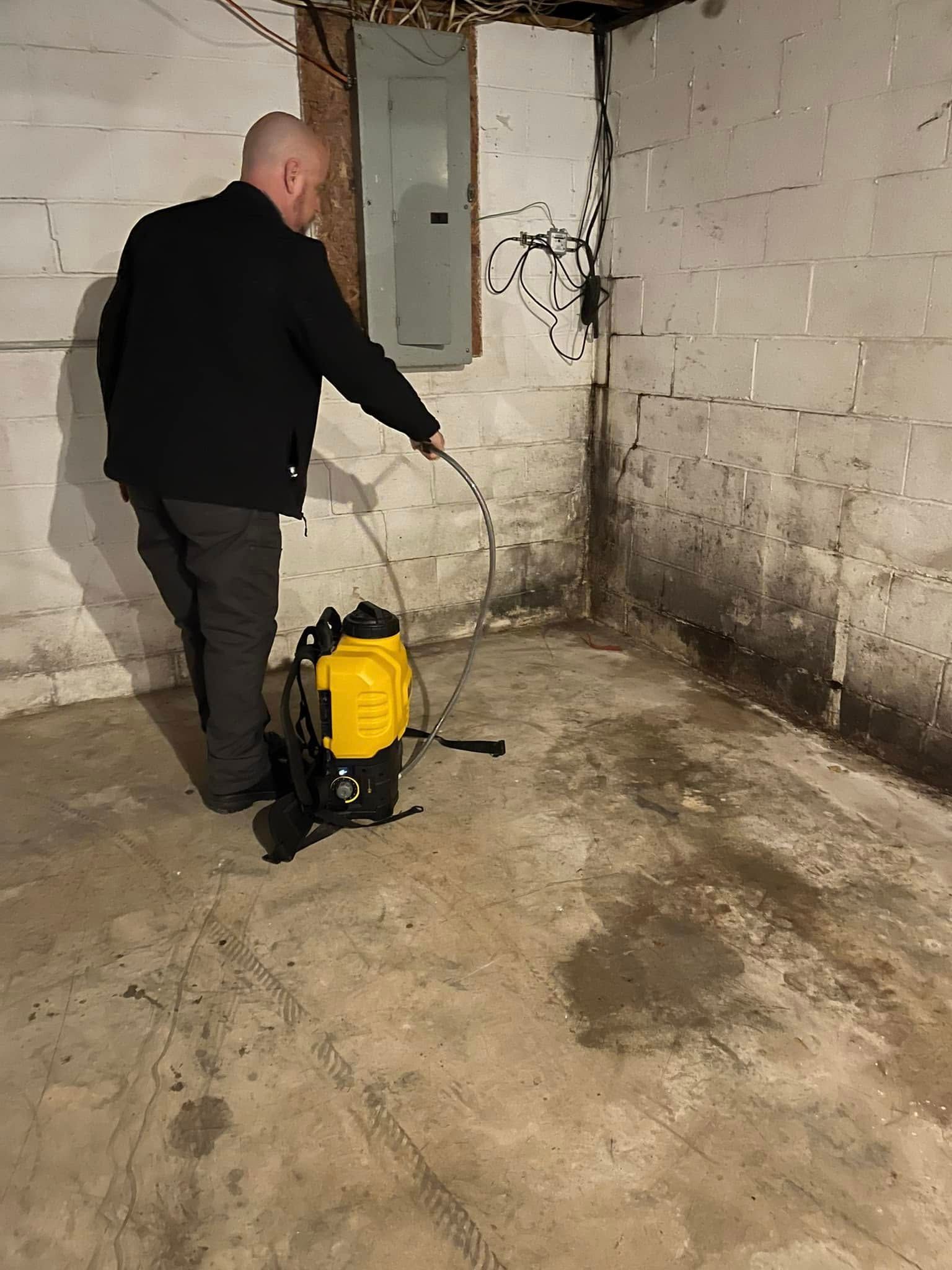 A man is spraying a wall with a sprayer in a basement.