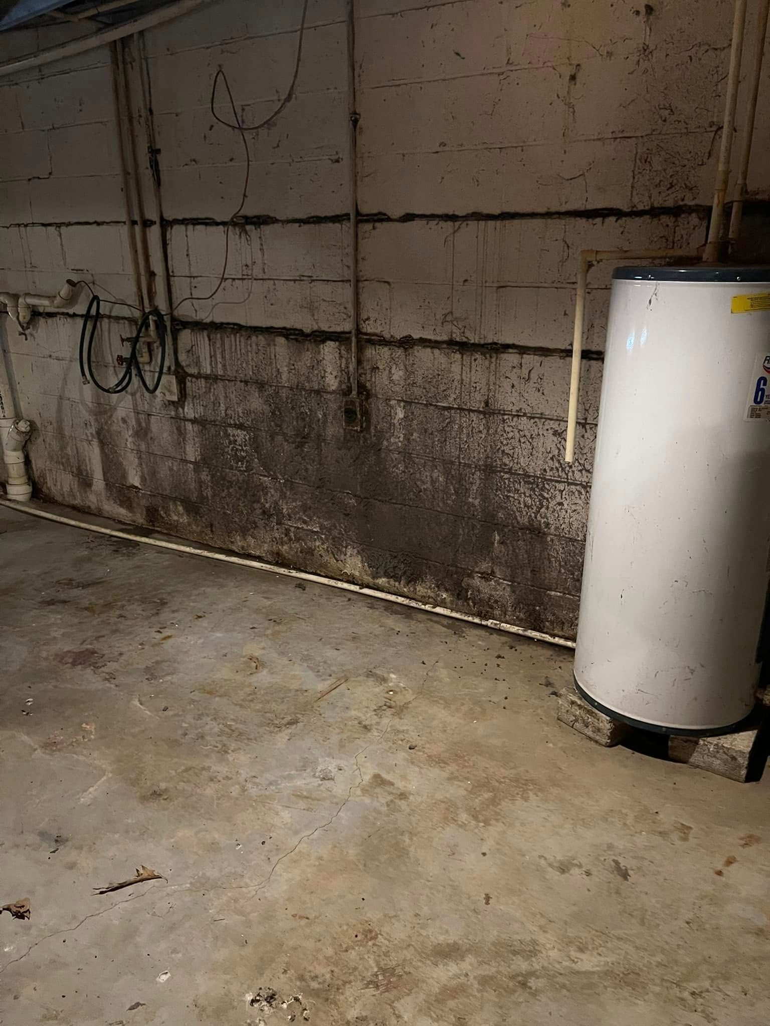 A white water heater is sitting in a basement next to a brick wall.