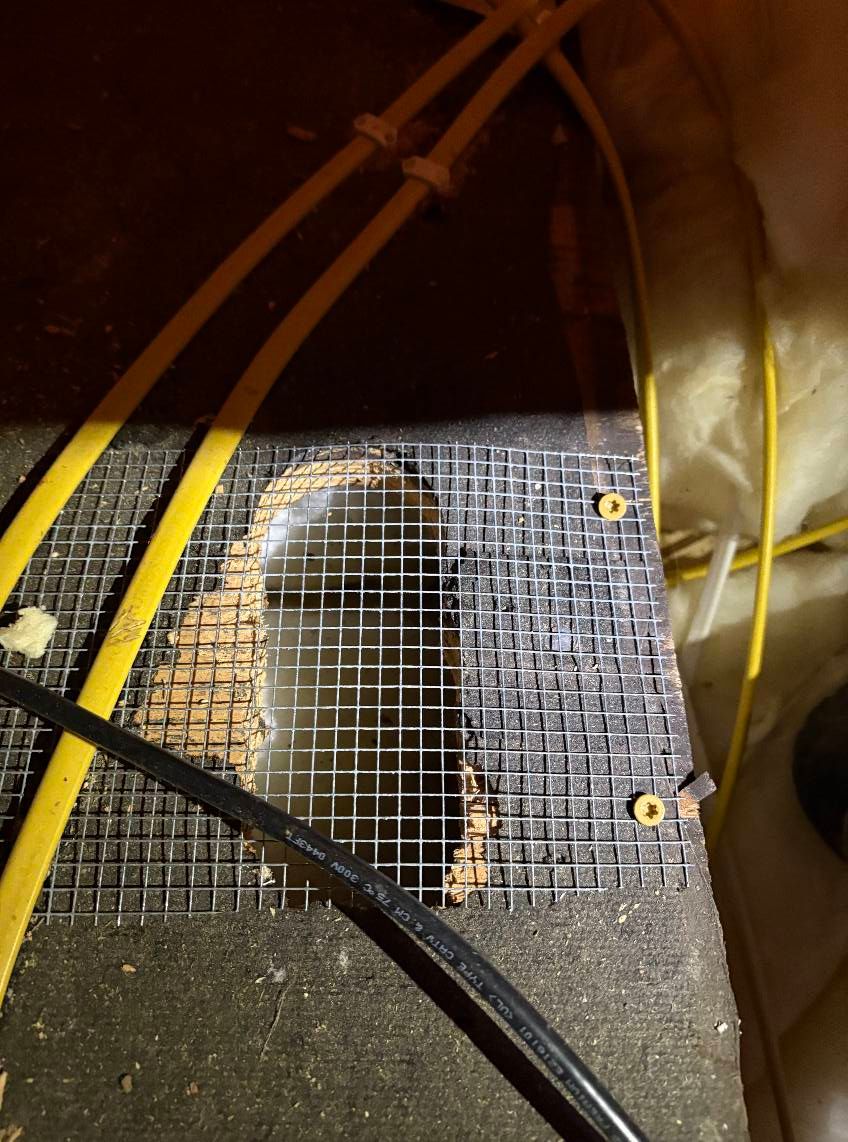 A hole in a wall with a wire mesh covering it