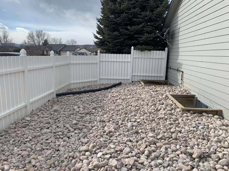 A white fence surrounds a pile of rocks in front of a house.