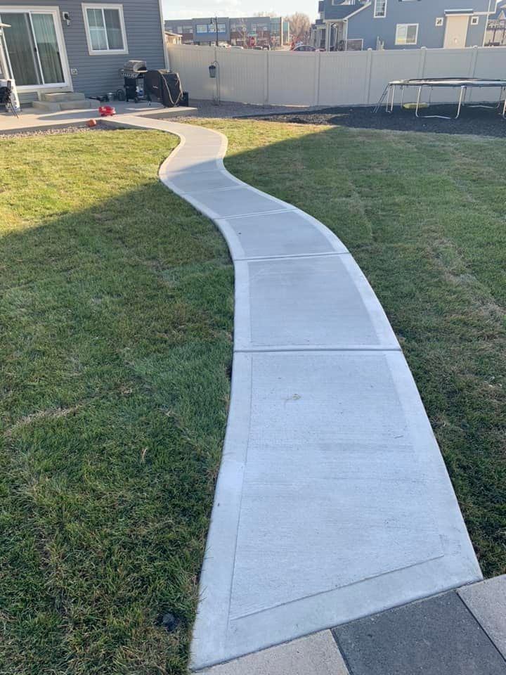 A concrete walkway leading to a house in a backyard.