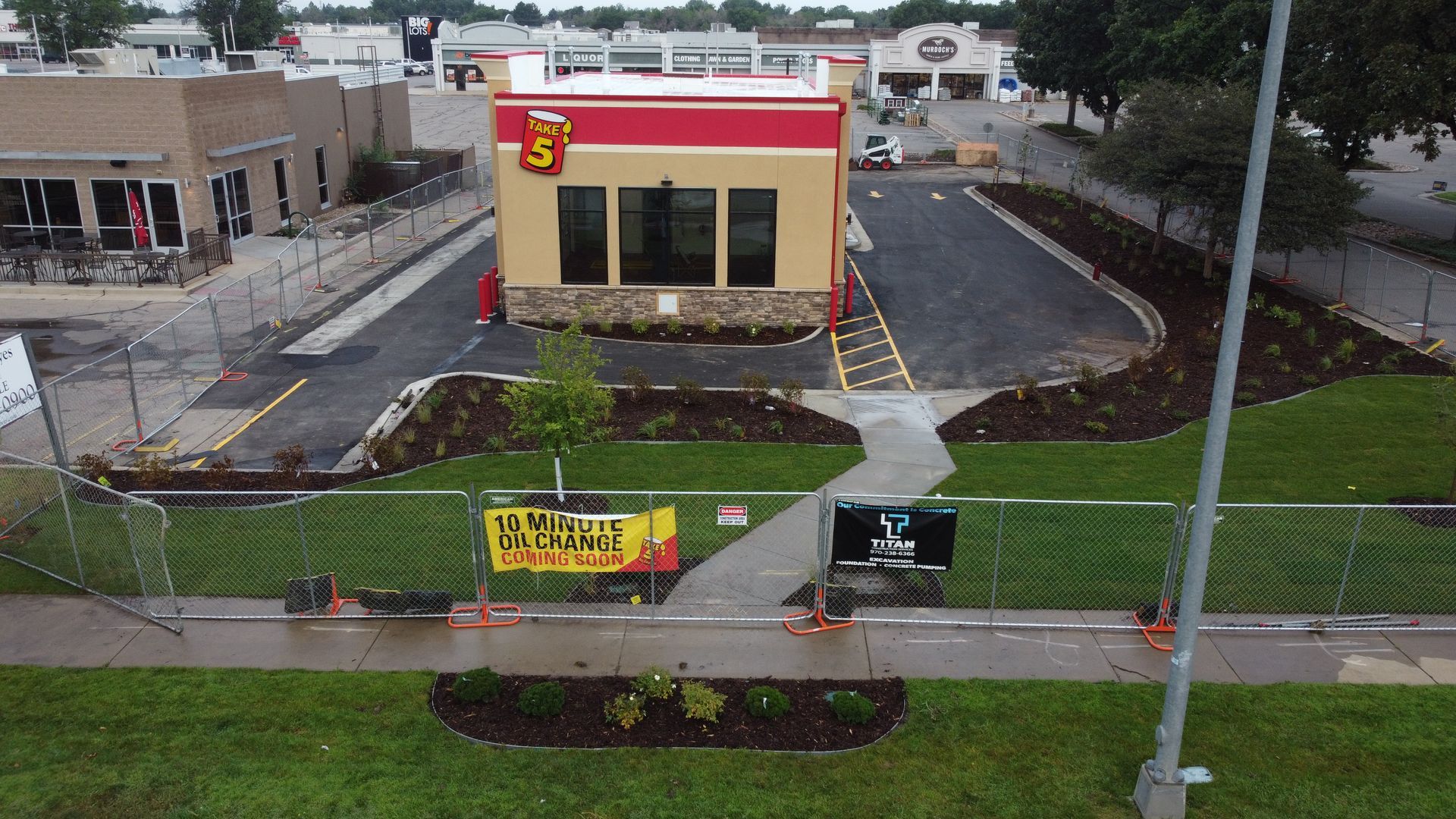 Exterior of a Taco John's restaurant under construction; red and tan building, new landscaping, and safety fencing.