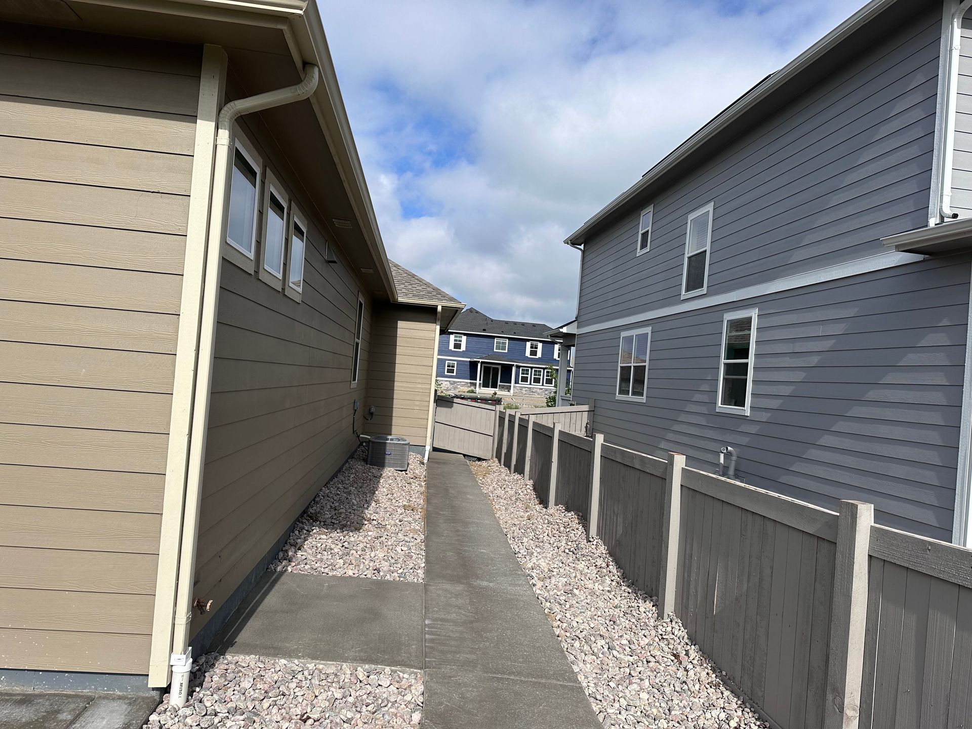 A narrow concrete walkway between two houses, with a gravel bed and fence on either side.