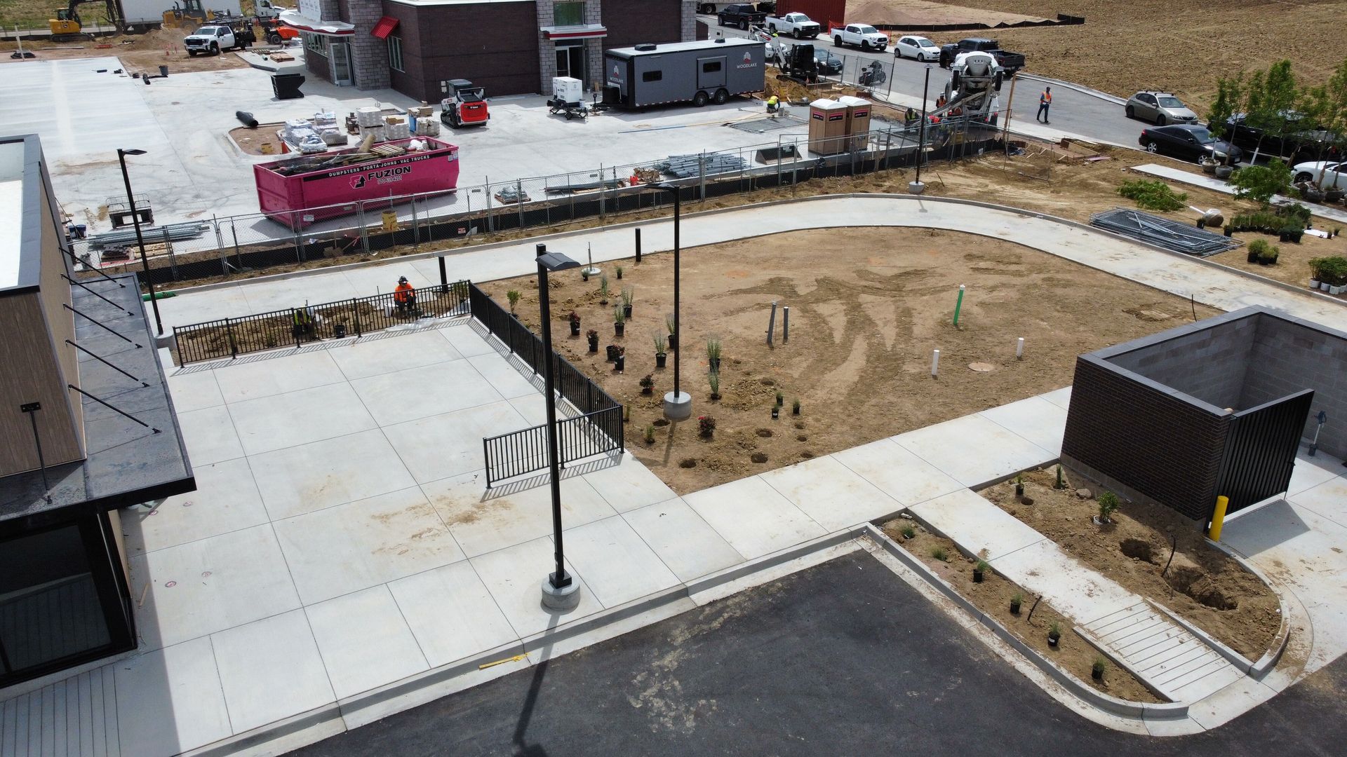 Construction site with paved areas, dirt patches, and buildings in the background. Several construction vehicles are present.